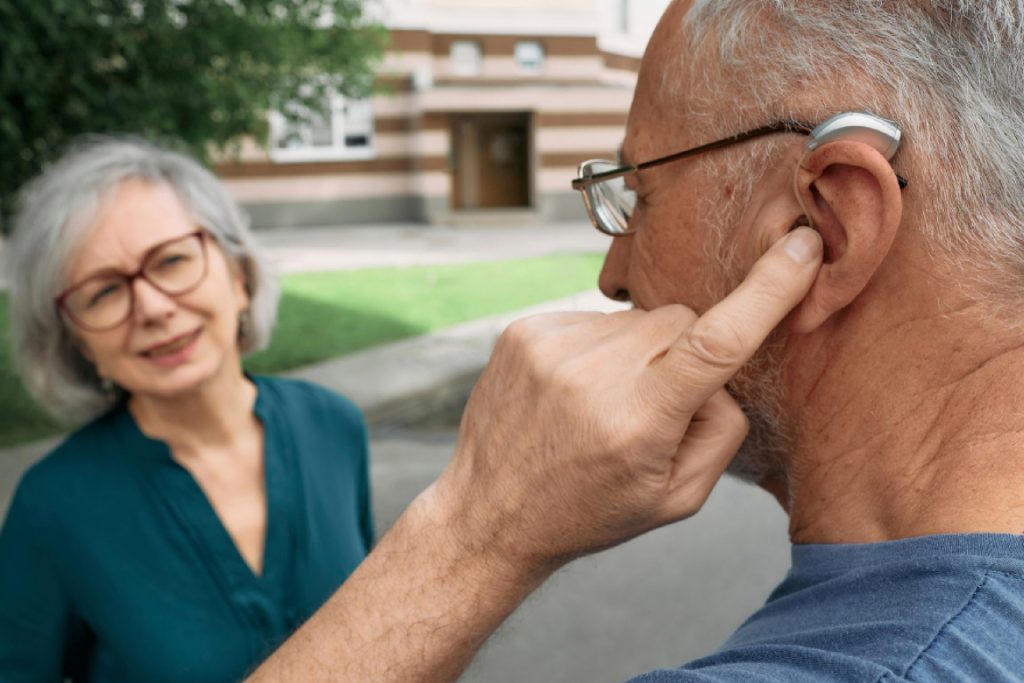 Senior man adjusting a modern behind-the-ear (BTE) hearing aid fitted by Better Hearing Co.