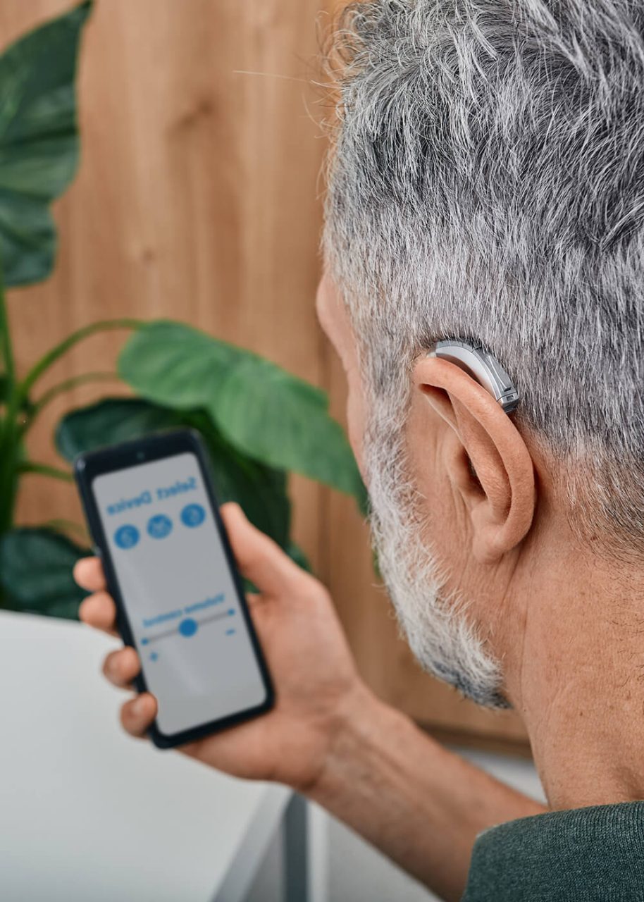 Man controlling his Bluetooth-connected digital hearing aid settings using a smartphone app.